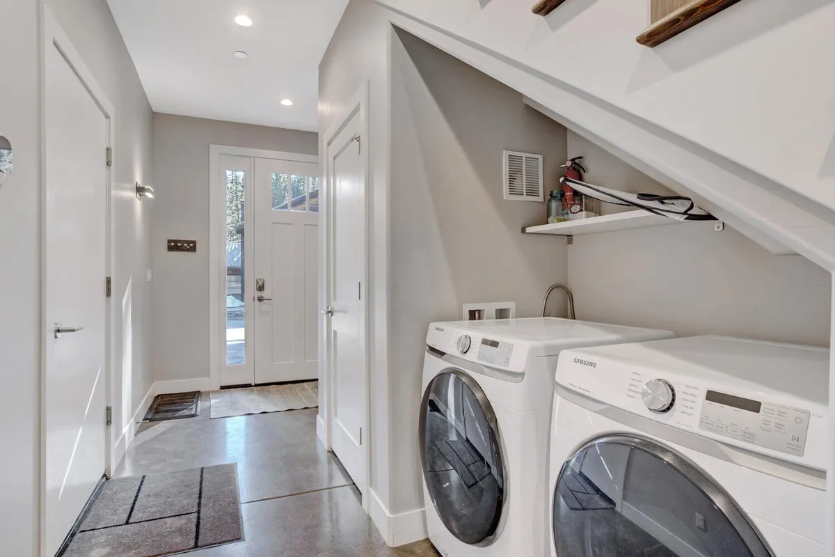 This interior scene centers on the laundry area, featuring a modern washer and dryer and the nearby front door. The space is well-lit and organized, underscoring practicality and convenience for guests managing ski gear or outdoor clothing.