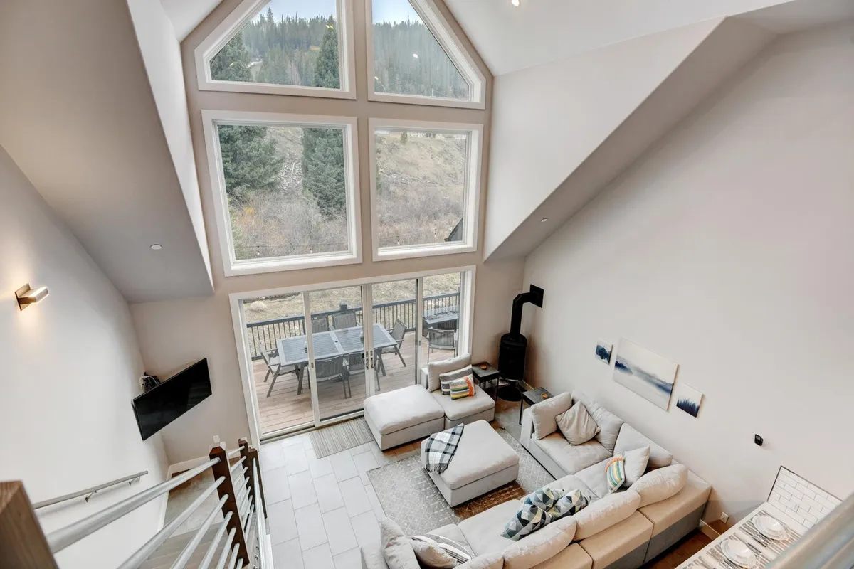 This interior shot offers a wide perspective on a modern sectional sofa with large windows that open onto a deck with dining area. The space is filled with natural light and offers stunning nature views, underlining the sense of openness and connection.