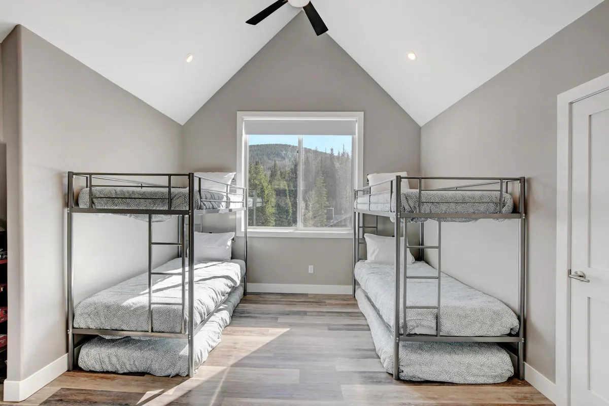 A cozy bunk room with two sets of bunk beds, a large window offering mountain views, and space for sleeping, reading, or playing games. The room feels lively yet comfortable, ideal for children or groups of friends.