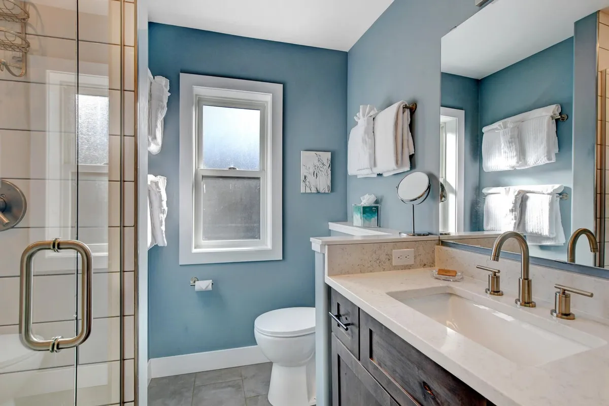A spa-like bathroom with a modern vanity and sink, a spacious shower area, plenty of natural light through a window, and fluffy towels on a rack. The design feels fresh, inviting, and perfect for self-care routines.