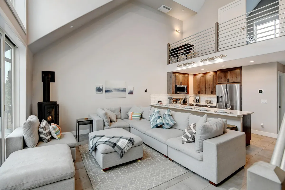 The scene showcases a comfortable living area with a large sectional sofa facing a fireplace, adjacent to an open kitchen. Artwork adds a designer touch, and the overall ambiance is welcoming, perfect for game nights or movie streaming as described in the section.