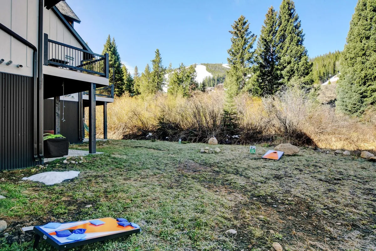 A spacious deck surrounded by mature trees, featuring cornhole game boards and a panoramic view of the mountains in the background. The atmosphere is peaceful and inviting, with plenty of open space for pets and people to relax after a day of outdoor activities.